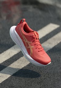 Chaussure de sport rouge avec un dessus texturé, une semelle blanche et des accents orange. Design léger avec des lacets et un col rembourré.