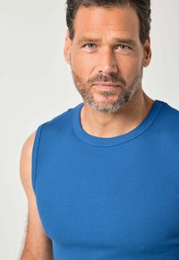 Modrý žebrovaný nátělník s kulatým výstřihem, s přiléhavým střihem. Tkanina vypadá hladká a měkká na dotek.