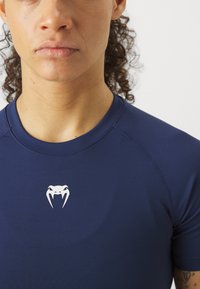 Kortsleeve marineblå treningsskjorte med hvit kobra-logo på brystet og sømløs design ved halslinning og skuldre.