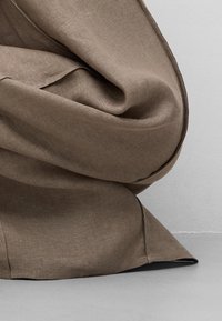 Tissu marron avec des plis visibles de couture sur une surface lisse gris clair.