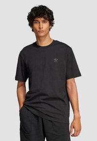 Fekete pamut póló rövid ujjakkal és kerek nyakkivágással. Az elülső részen egy kis, tónusos Adidas háromlevelű logó található.