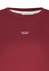 T-shirt à col rond côtelé bordeaux avec un petit logo brodé "GUESS JEANS" en blanc au centre de la poitrine.