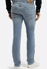 Jasnoniebieskie dżinsy o slim fit z tylnymi kieszeniami, delikatnym efektem przetarcia i kontrastowymi szwami. Noszone z białymi sneakersami.