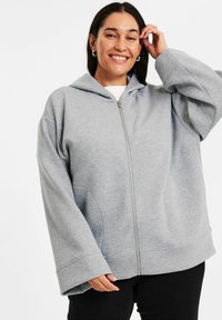Ljusgrå zip-up hoodie med huva, vida ärmar och sidofickor. Tillverkad av ett bekvämt material med en slät textur.