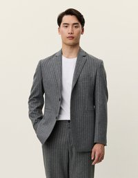 Γκρι κοστούμι με ρίγες, με κανονικούς γιακάδες, κλείσιμο με ένα κουμπί και δύο μπροστινές τσέπες, συνδυασμένο με λευκή μπλούζα από κάτω.