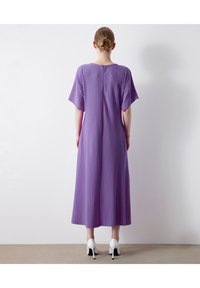 Lila plissiertes Kleid mit kurzen Ärmeln, rundem Halsausschnitt und Reißverschluss am Rücken. Kombiniert mit weißen High Heels.