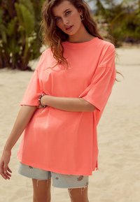 Maglietta oversize corallo brillante con maniche corte e scollo arrotondato. Abbinata a pantaloncini di denim azzurro chiaro, decorati con ricami floreali.