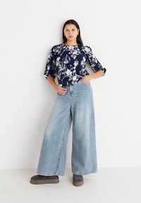 Blusa floreale blu navy con maniche a tre quarti abbinata a jeans a vita alta e gamba ampia di un lavaggio chiaro e calzature marroni scure.