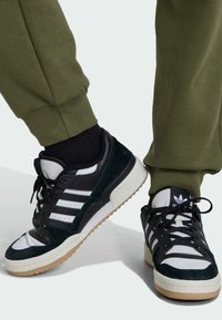 Crne i zelene suknjaste tenisice s bijelim detaljima, sa tri pruge, teksturiranom površinom i gumiranim potplatom u boji gume.