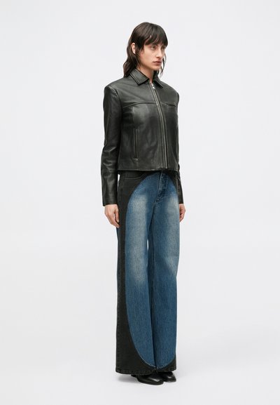 Giacca in pelle nera con collo a risvolto, chiusura con zip e design aderente, abbinata a jeans a gamba larga bicolore in denim blu e nero.