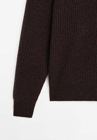Donkerbruin geribbelde sweater met een gestructureerde brei, lange mouwen en een aansluitende zoom. De stof lijkt zacht en warm te zijn.