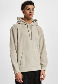 Beige, ribbet genser med kengurulomme, snorhette og teksturert stoff. Har lange ermer og en avslappet passform.