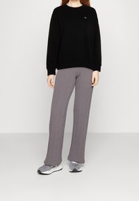 Schwarzer Sweatshirt mit gerippten Bündchen und kleinem Logo, kombiniert mit hellgrauen, gerippten, weit geschnittenen Hosen und grauen Sportschuhen.