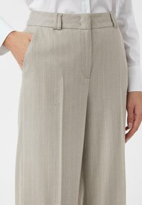 Jasnoszare spodnie w prążki o dopasowanym kroju, z przednimi kieszeniami i subtelnym połyskiem. Tkanina wydaje się mieć fakturę i być gładka.