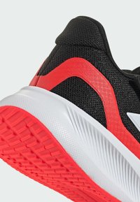 Baskets de sport noires avec des accents rouges, un dessus texturé et une semelle en caoutchouc avec un motif de grip distinct. Conception pour un maintien sûr.