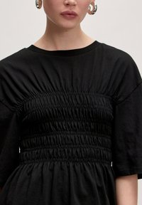 Zwarte jurk met een geplooide bodice met smocking, korte mouwen en een vloeiende rok. Zachte stoftextuur met een gladde afwerking.
