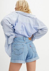 Camisa a rayas azul claro con mangas abullonadas, combinada con shorts de mezclilla de tiro alto. Los shorts tienen un dobladillo enrollado y bolsillos traseros visibles.