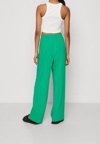 Zelené široké kalhoty vyrobené z lehkého materiálu, s elastickým pasem, kombinované s bílým, bezramínkovým cropped topem.