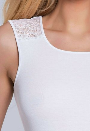 Zbliżenie na biały bezrękawnik z koronkowymi zdobieniami na ramieniu, noszony przez osobę o blond włosach.