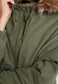 Olive green parka with a fur-lined hood, featuring a zip closure, adjustable drawstrings, and textured fabric.