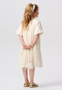 Kremowa sukienka z bufkami, teksturowany materiał, falbaniasty dół i pasująca torebka na sznurku; w zestawie z błyszczącymi złotymi balerinkami.
