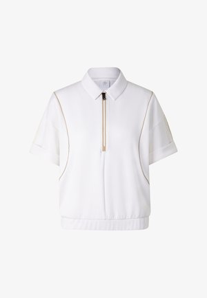 Chemise blanche à manches courtes avec col, fermeture éclair devant, passepoil beige sur les côtés, petite poche sur chaque manche, ourlet élastique en bas.