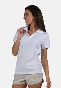 Polo blanc avec un col et des accents de poignets roses, associé à un short coloré présentant un motif floral et une bordure rose.