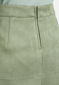 Jupe en daim vert clair avec fermeture éclair latérale et détails de couture, portée avec un haut vert clair.