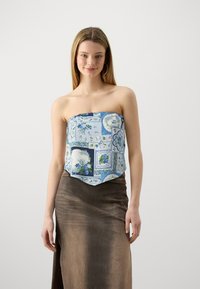Top senza spalline in stampa floreale blu con motivi quadrati e rotondi, abbinato a una lunga gonna marrone in tessuto seta con una texture liscia e uno spacco laterale.