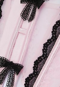 Rosa satin korsett med svart spetskant, med delikata rosetter. Texturen inkluderar slät satin och intrikata spetsdetaljer.