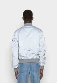 Light blue bomber jacket with ribbed gray collar and cuffs, featuring a smooth, shiny texture and side pockets.