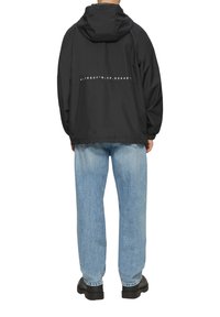 Zwarte, lichtgewicht jas met een capuchon, met een gedrukt coördinatendesign op de achterkant. Gepaard met lichtgewassen denim jeans en zwarte schoenen.