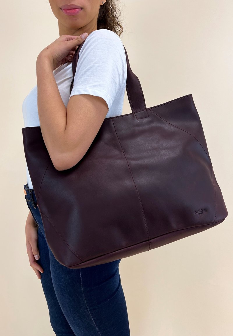 Dark burgundy leather tote bag with smooth texture, rectangular shape, and sturdy handles. Features subtle stitching and a logo on the side.