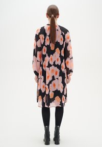 Blommig plisserad klänning i svart med rosa och orange mönster. Långa ärmar och knälång, tillsammans med svarta ankelstövlar. Slät textur.