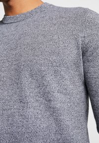 Szary sweter z dzianiny o teksturowanej powierzchni, z okrągłym dekoltem i długimi rękawami, zaprojektowany z myślą o komforcie i łatwości noszenia.