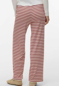 Personne portant un pantalon ample à rayures horizontales rouges et blanches, associé à des chaussures beiges et un haut à manches longues blanc.
