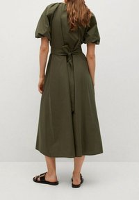 Olivengrünes Kleid mit puffigen kurzen Ärmeln, einem Bindeband am Rücken und einem fließenden, knielangen Rock. Texturiertes Material, lässiger Schnitt.