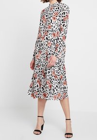 Långärmad midiklänning i vitt med svart leopardmönster och rosa blommiga detaljer. Utsvängd silhuett, lätt tyg och knapprad.