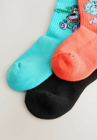 Tres pares de calcetines: uno turquesa, uno naranja con un diseño y uno negro. Todos son de tejido de punto, con textura de canalé y punteras redondeadas.