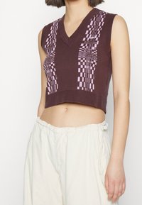 Brown cropped sweater with a V-neck, featuring a geometric pattern in lavender. Made from a soft, knitted material.