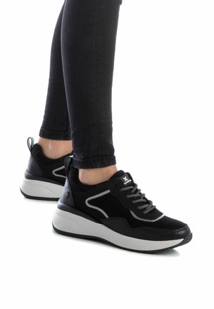 Zapatillas deportivas negras con una suela blanca gruesa, parte superior de ante y textil, detalles en gris y cordones negros, combinadas con unos vaqueros skinny negros.