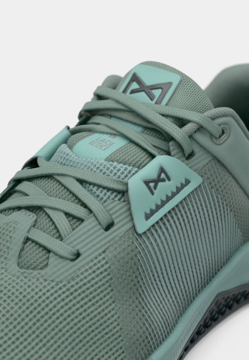 Zapatilla deportiva verde claro con una parte superior de malla texturizada, acentos en menta en contraste y patrones geométricos intrincados en la puntera.