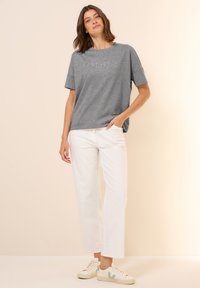 Grijze T-shirt met korte mouwen met de tekst "ESTHETIC", gecombineerd met witte wijde broek en witte sneakers met groene accenten.