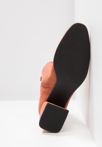 Suède enkelboot in koraal met een blokhak en een ritsdetail aan de zijkant. Zwarte gestructureerde zool. Soepele, matte afwerking.