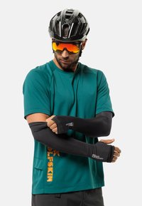 Schwarze Armsleeves aus Stretchstoff, die über einem türkisfarbenen Sportshirt mit einem Logo in Orange getragen werden. Modell trägt Sonnenbrille und einen Helm.