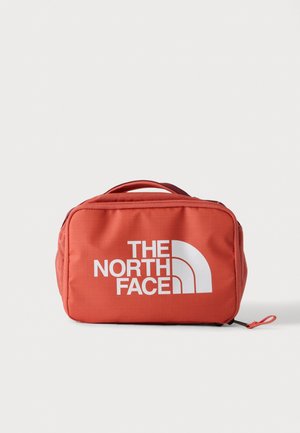 Bolsa roja rectangular compacta con asa superior y gran logo blanco de The North Face en el frente, mostrada sobre un fondo claro y liso.