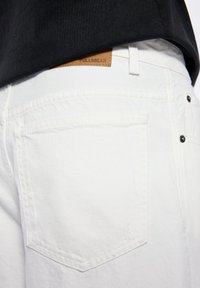 Jeans de denim blanco con un acabado texturado, que presentan un bolsillo trasero y una pestaña de cuero marrón etiquetada "PULL&BEAR" en la cinturilla.