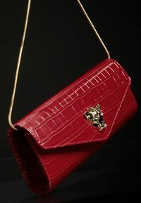 Czerwona torebka kopertówka z faux krokodylowej skóry z złotym łańcuszkiem i dekoracyjnym akcentem czaszki w kolorze czarnym i złotym na przodzie. Teksturowana powierzchnia.