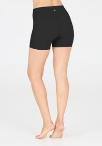 Shorts de sport noirs avec une taille haute, une texture lisse et un logo en accent à l'arrière. Coupés au-dessus du milieu de la cuisse, conçus pour la flexibilité.