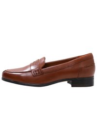 Mocassin en cuir marron avec un bout arrondi, des accents cousus et un talon bloc bas. Finition lisse avec un éclat subtil.